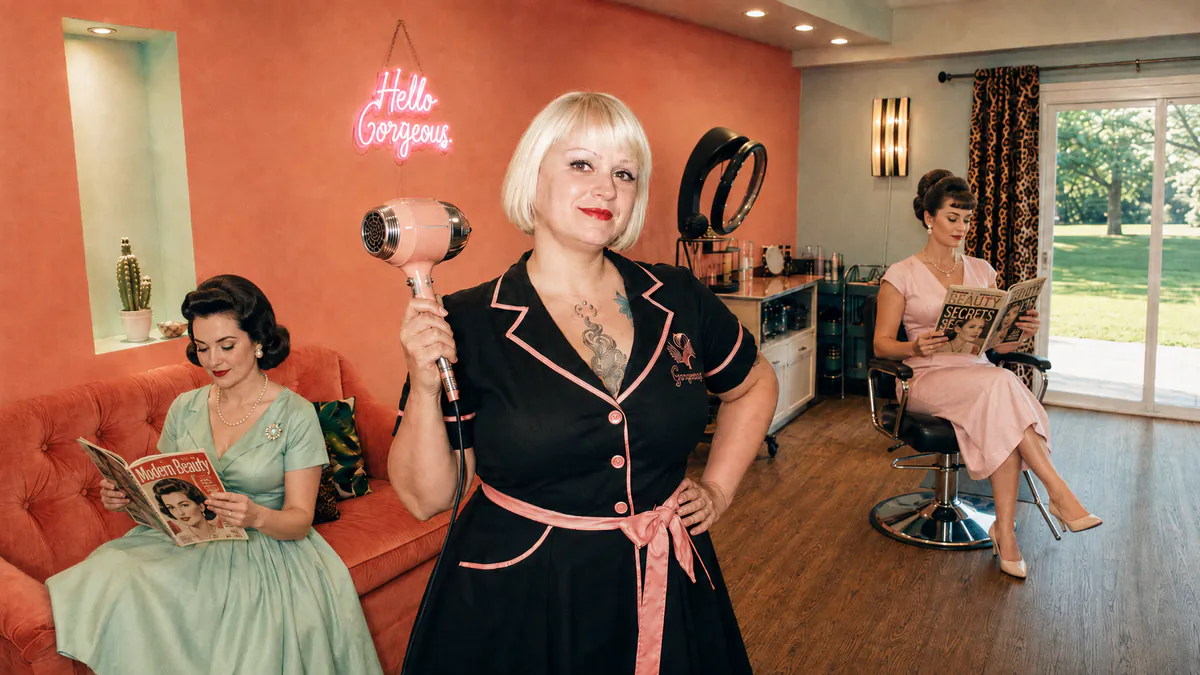 Miranda holding a pink vintage hair dryer in her retro salon.